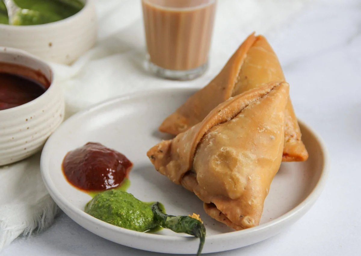 Golden Punjabi samosas on a plate with mint chutney